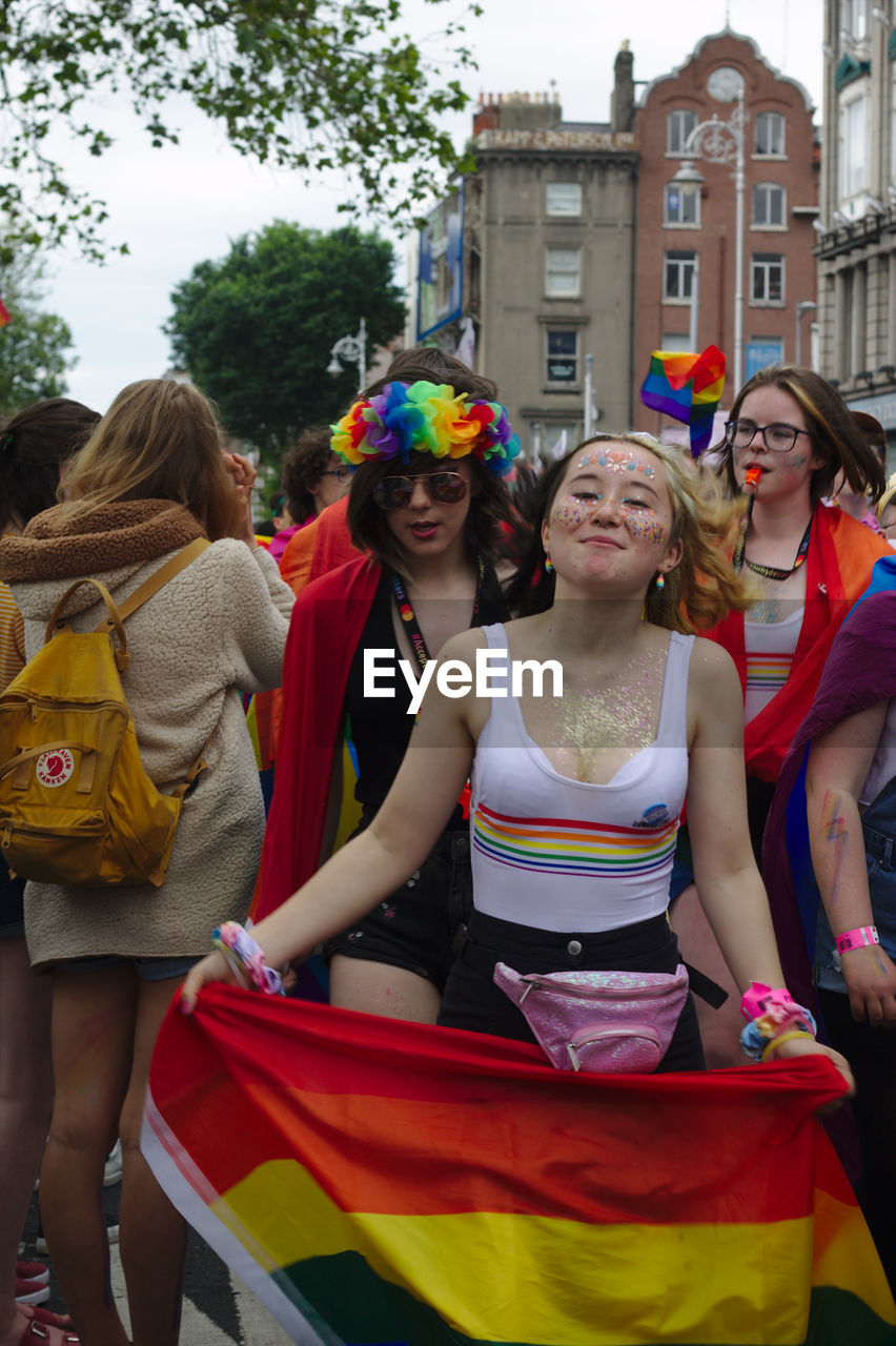 PORTRAIT OF SMILING YOUNG WOMEN STANDING AGAINST PEOPLE