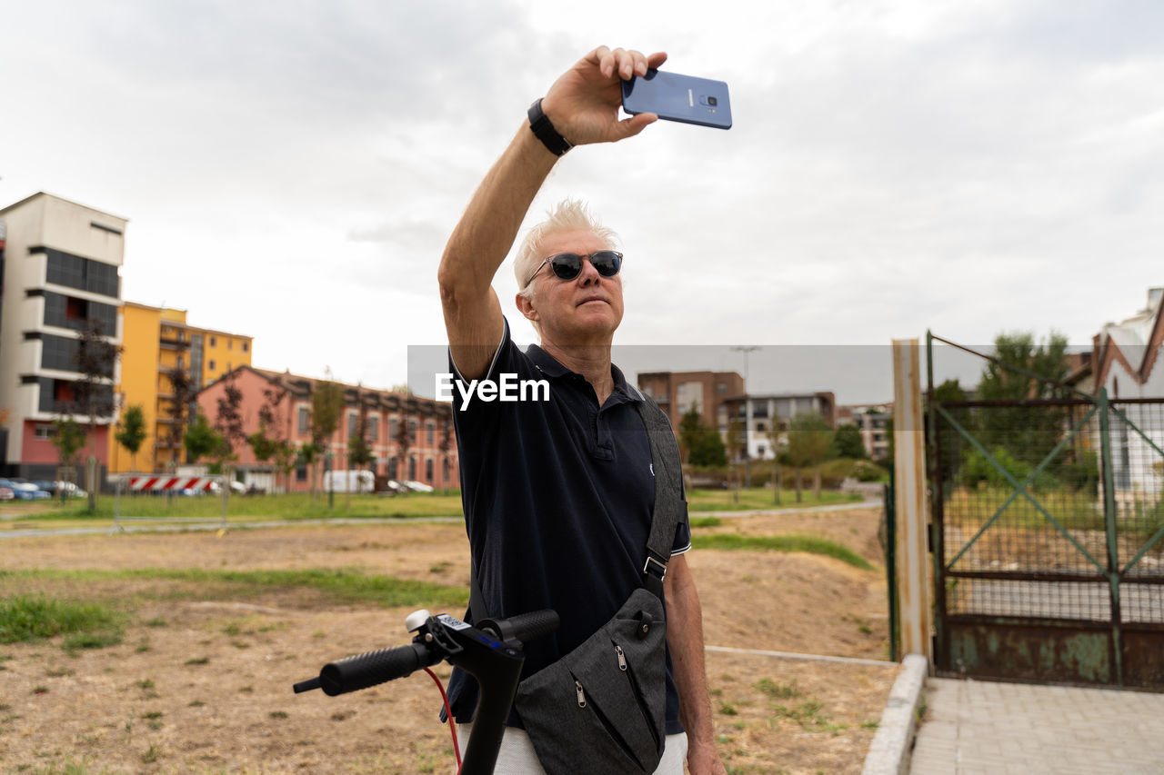 Commuter hipster man with electric scooter take a selfie with smartphone in the suburbs