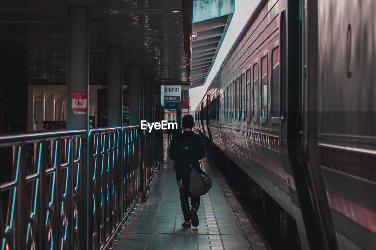 REAR VIEW OF MAN WALKING AT RAILROAD STATION