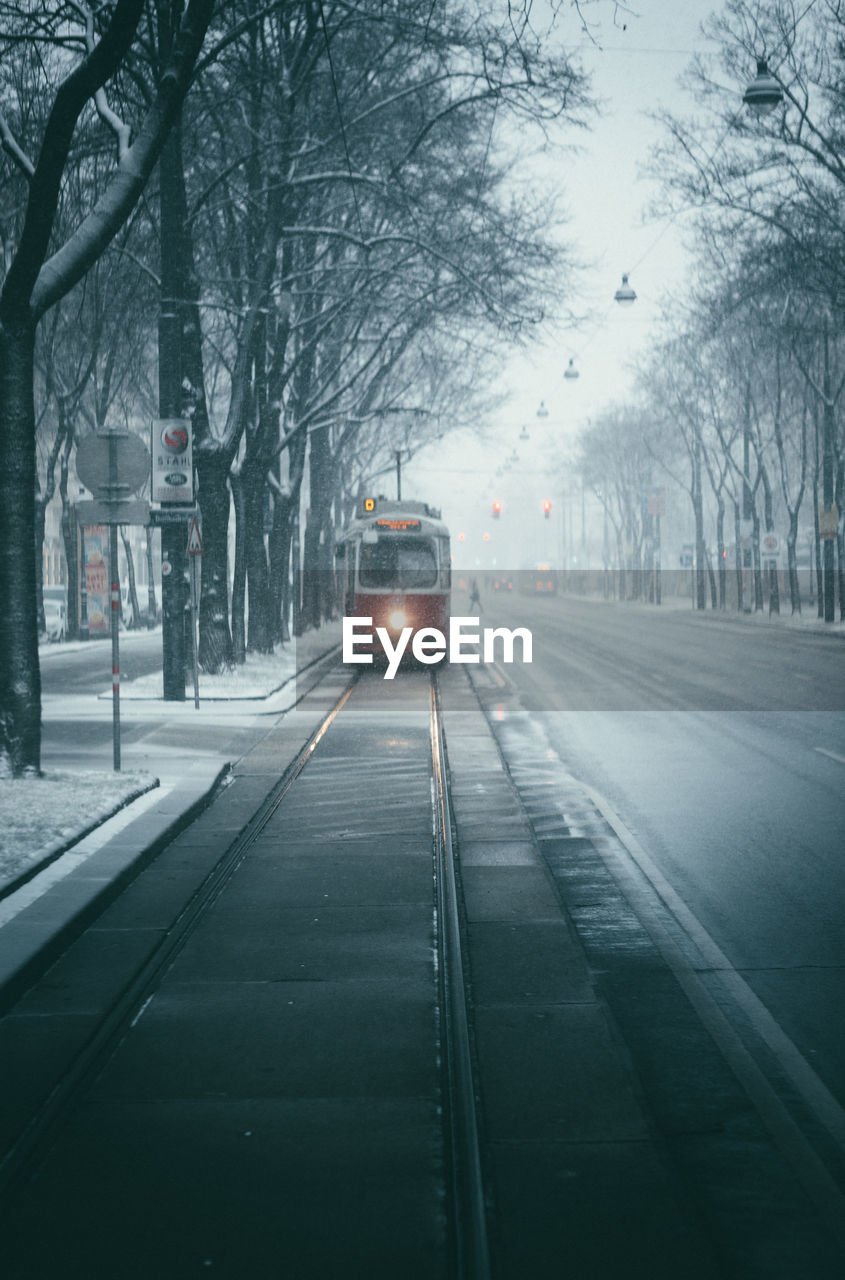 A retro tram with its headlights on during a snowfall moves towards