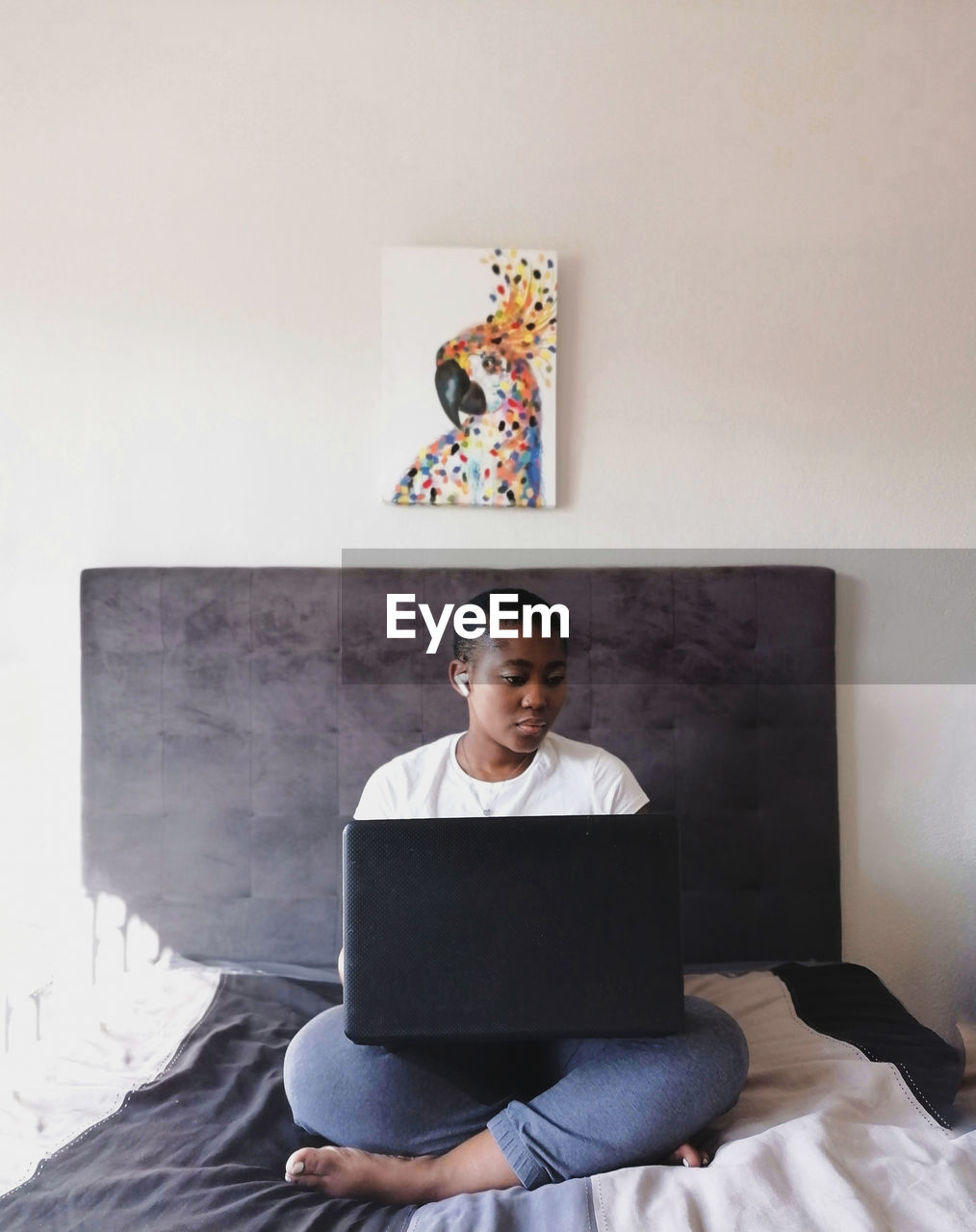 Black woman using laptop while sitting on bed at home