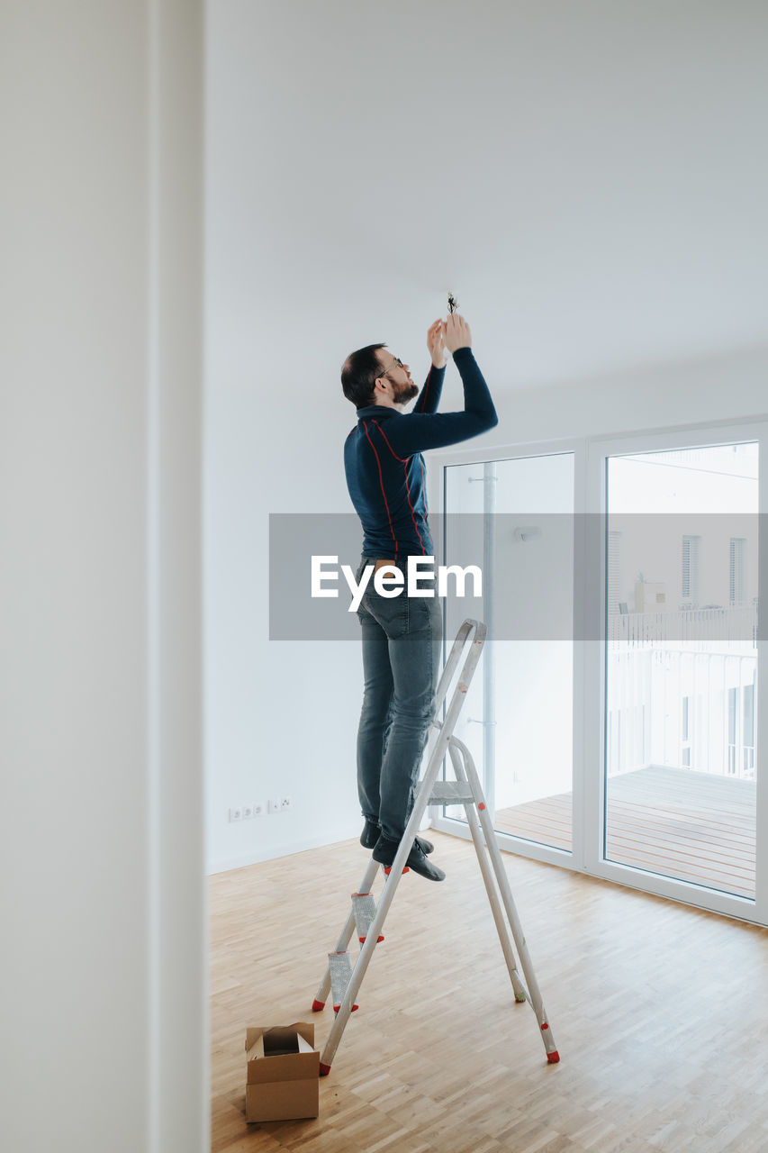 Home owner standing on ladder fixing light installation