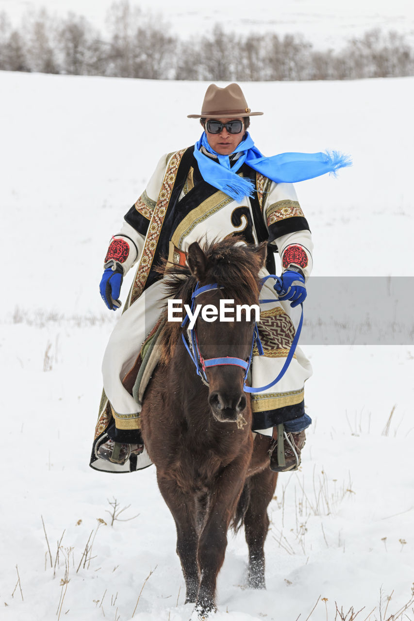 PORTRAIT OF MAN RIDING HORSE ON FIELD