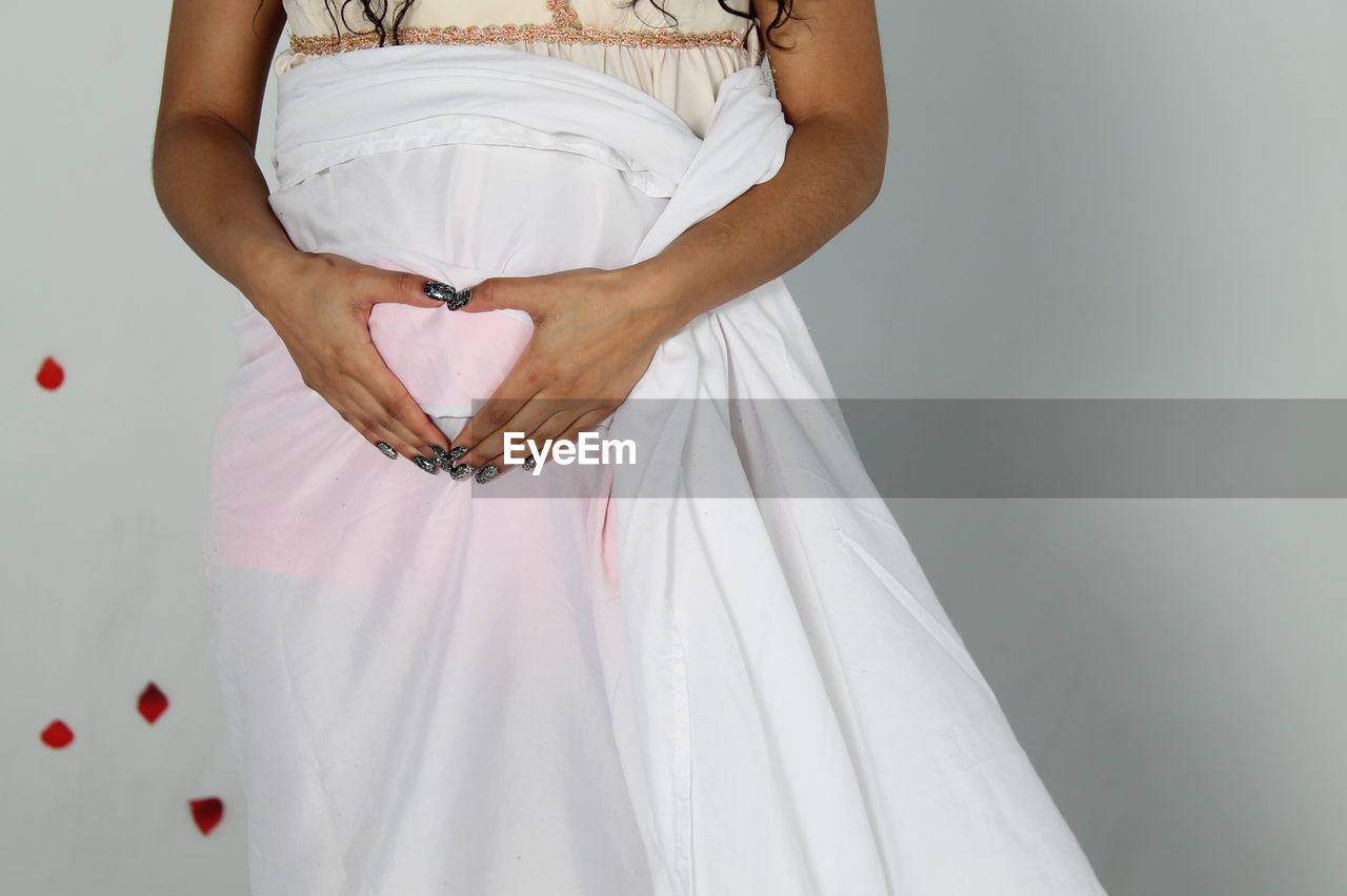 Midsection of pregnant woman with hands on stomach against wall