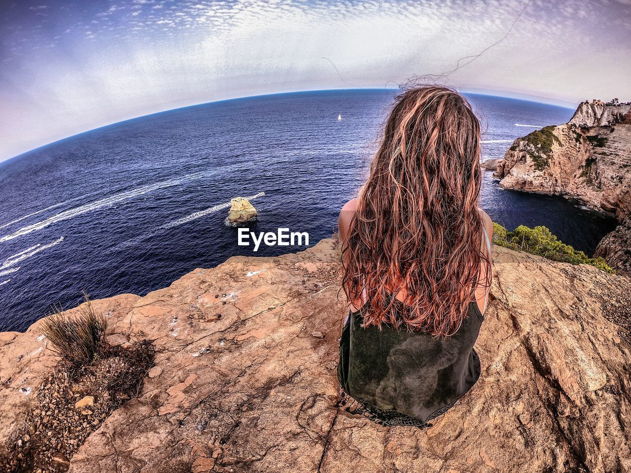 REAR VIEW OF WOMAN LOOKING AT SEA AGAINST ROCK