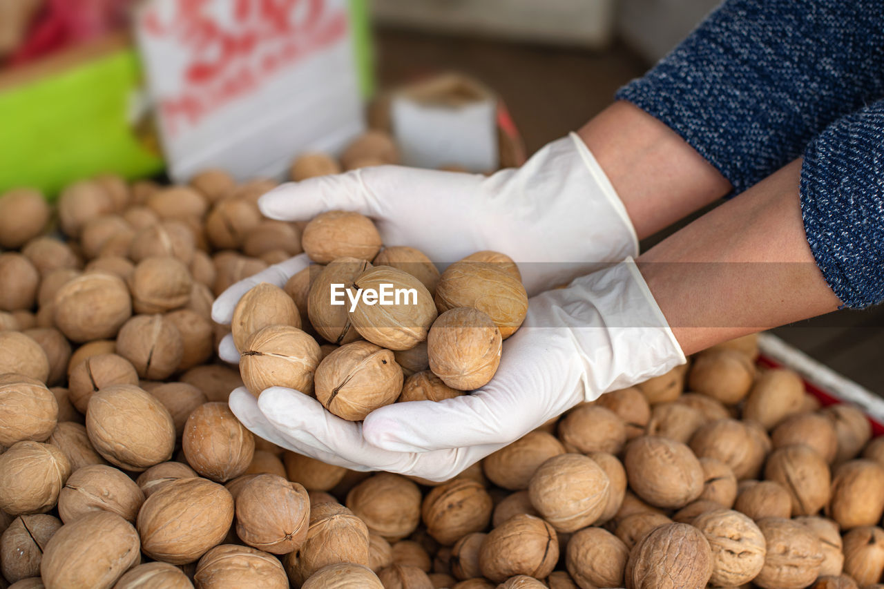 Close-up of hands in gloves for sale at market stall. buying walnuts