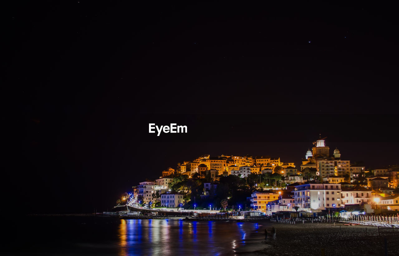 Beach by illuminated buildings at night