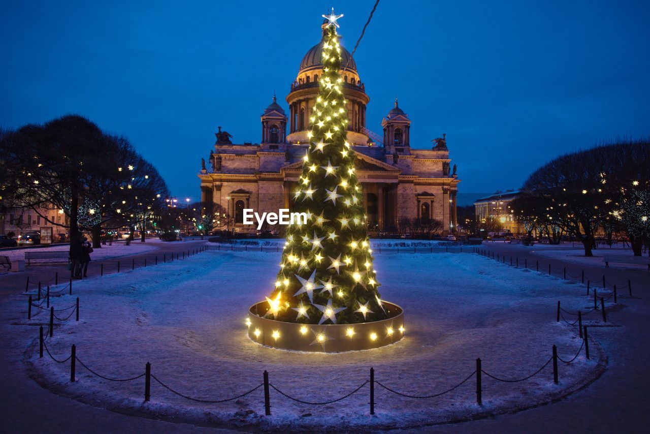 Illuminated christmas tree on snow covered field against saint isaac cathedral