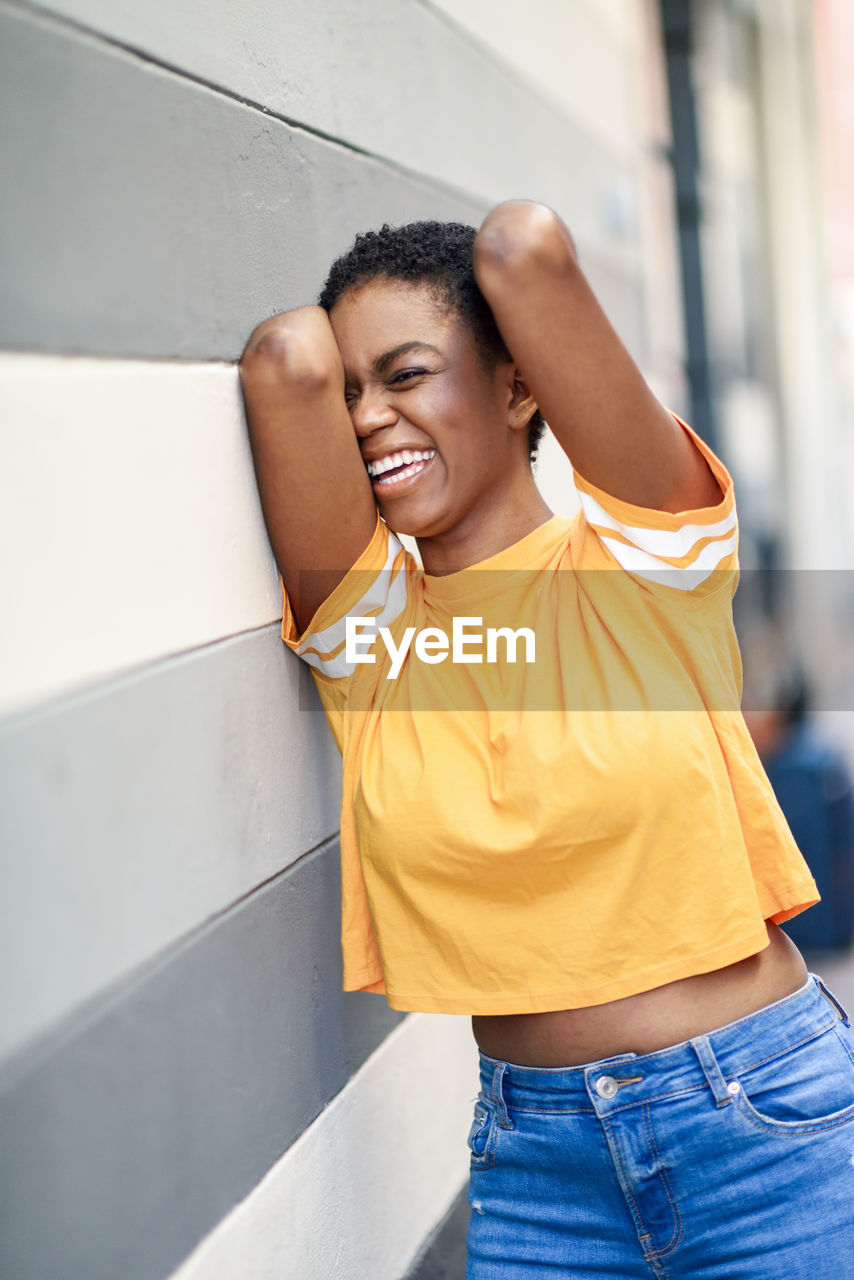 Cheerful young woman standing by wall