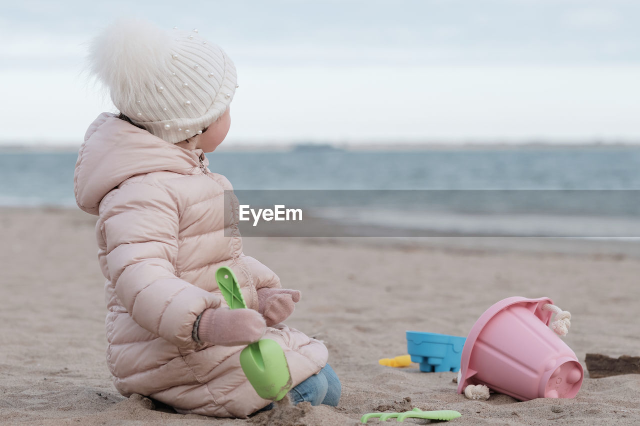 Little girl is digging in the sand on a cold day at the beach