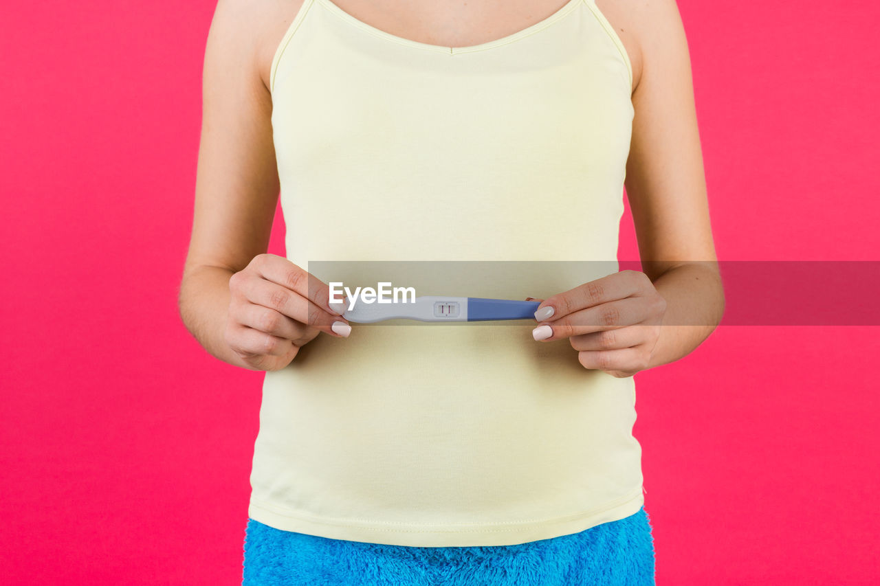 MIDSECTION OF WOMAN HOLDING PINK DRESS