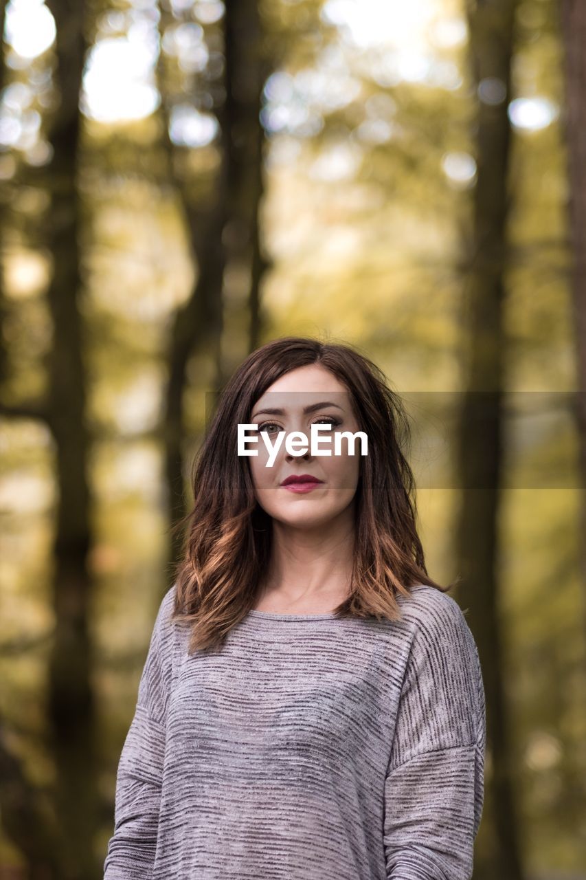 Portrait of young woman standing against trees at forest