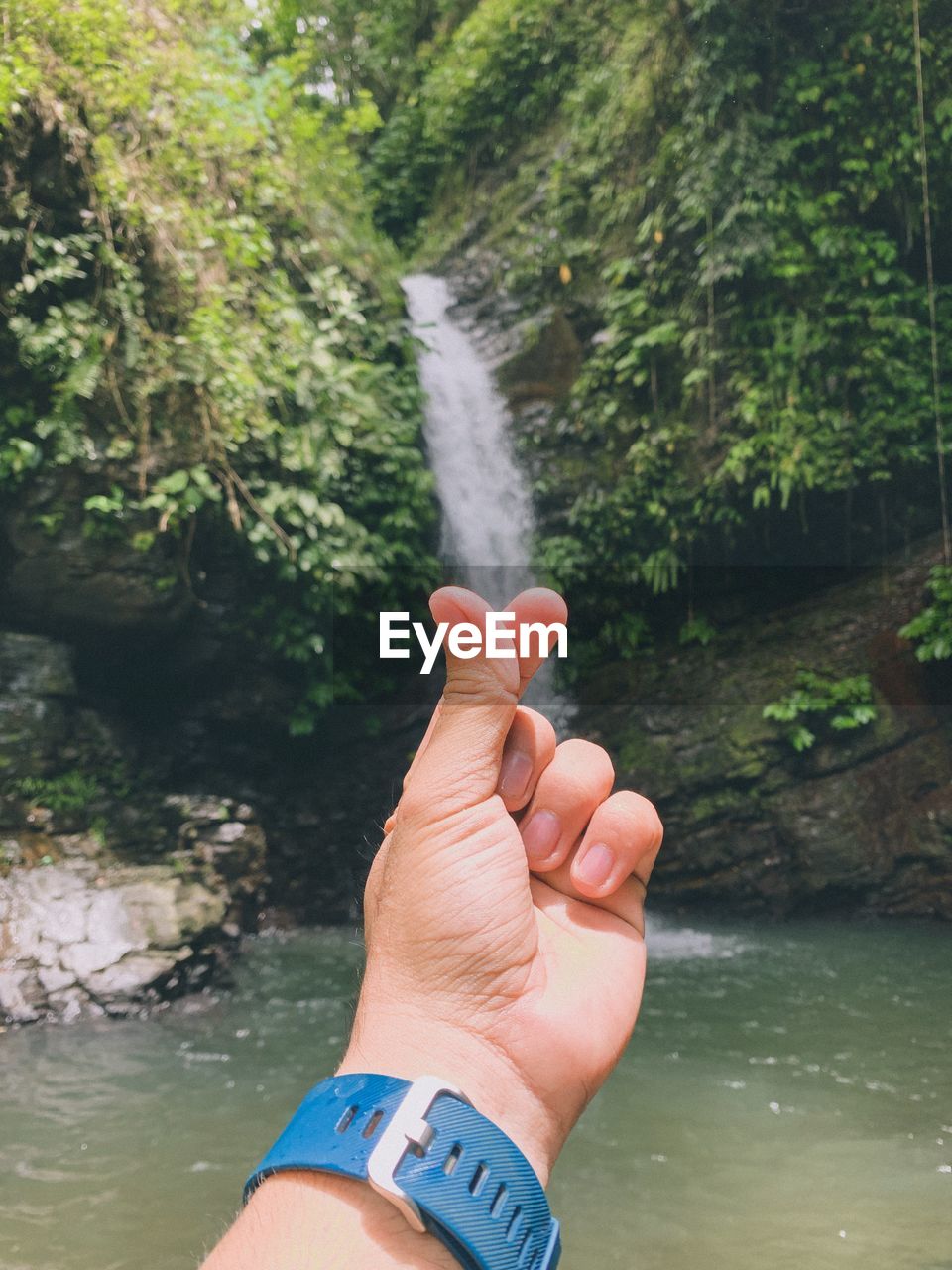 CROPPED IMAGE OF HAND AGAINST WATERFALL