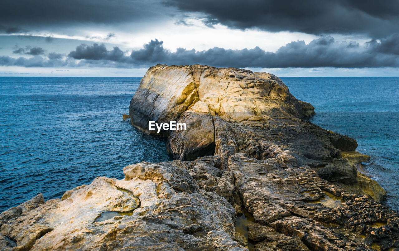 Rock formation on sea shore against sky