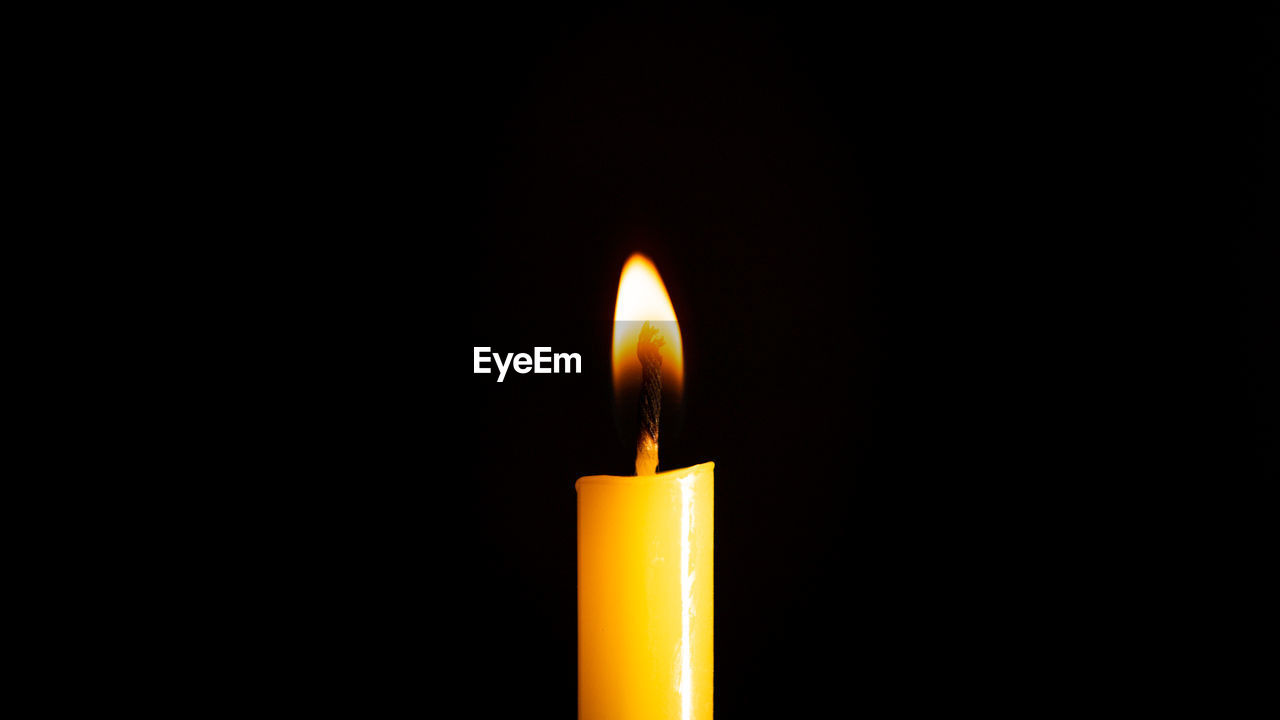 CLOSE-UP OF LIT CANDLE IN DARK