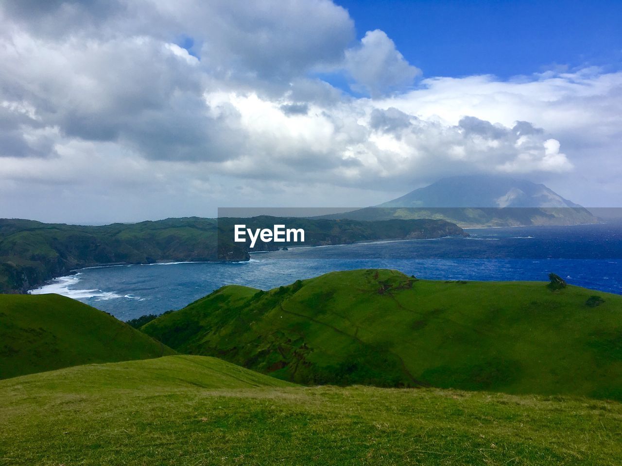 Scenic view of grassy field by sea against cloudy sky 