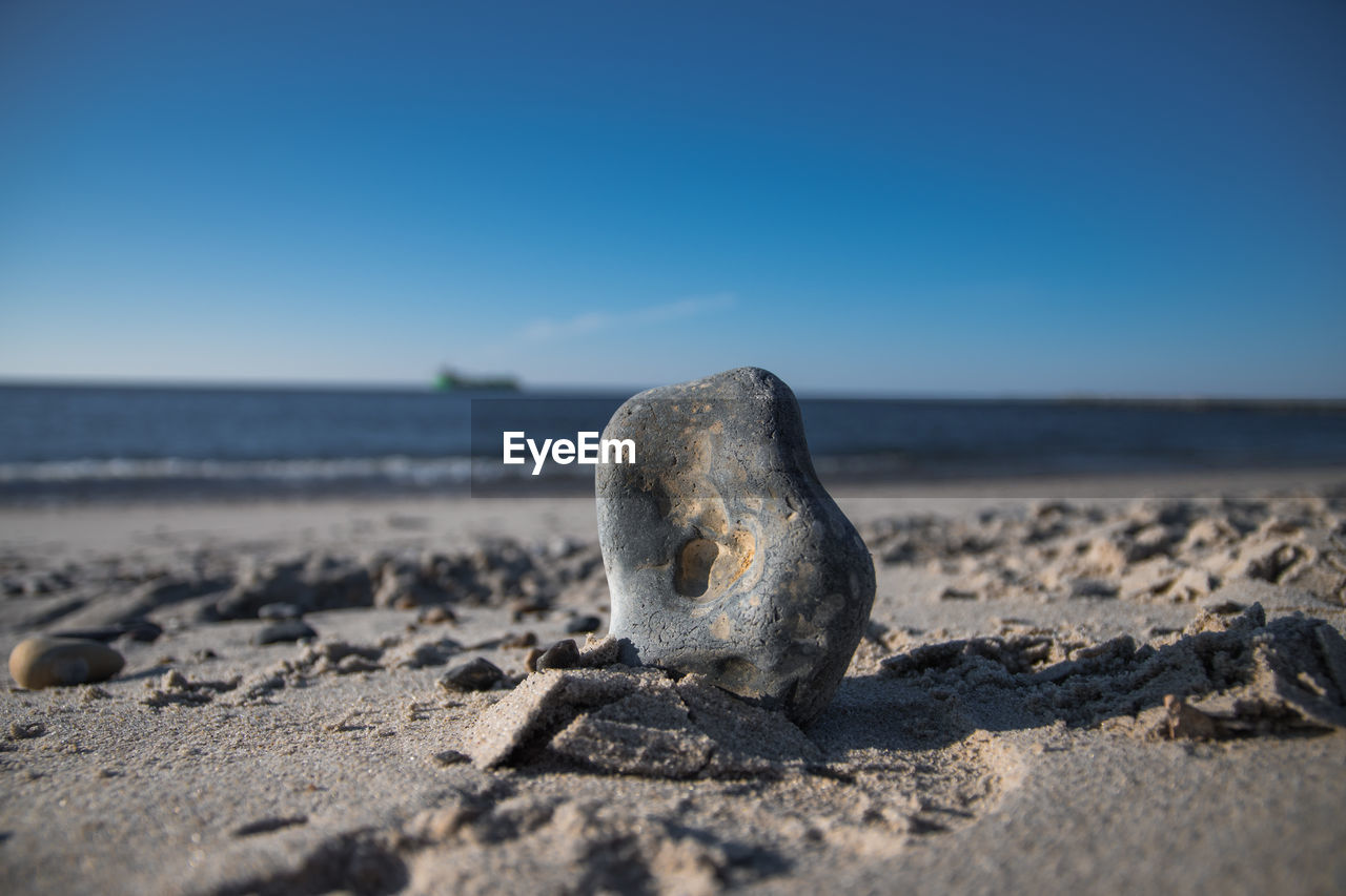 CLOSE-UP OF PEBBLES ON SAND AT BEACH AGAINST CLEAR SKY