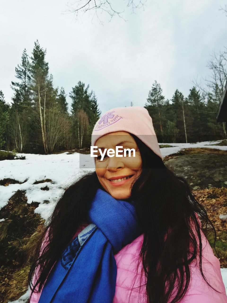 PORTRAIT OF SMILING YOUNG WOMAN IN SNOW AGAINST TREES