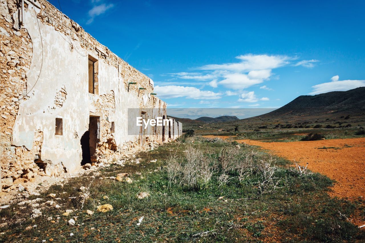 Abandoned building by field against sky in desert