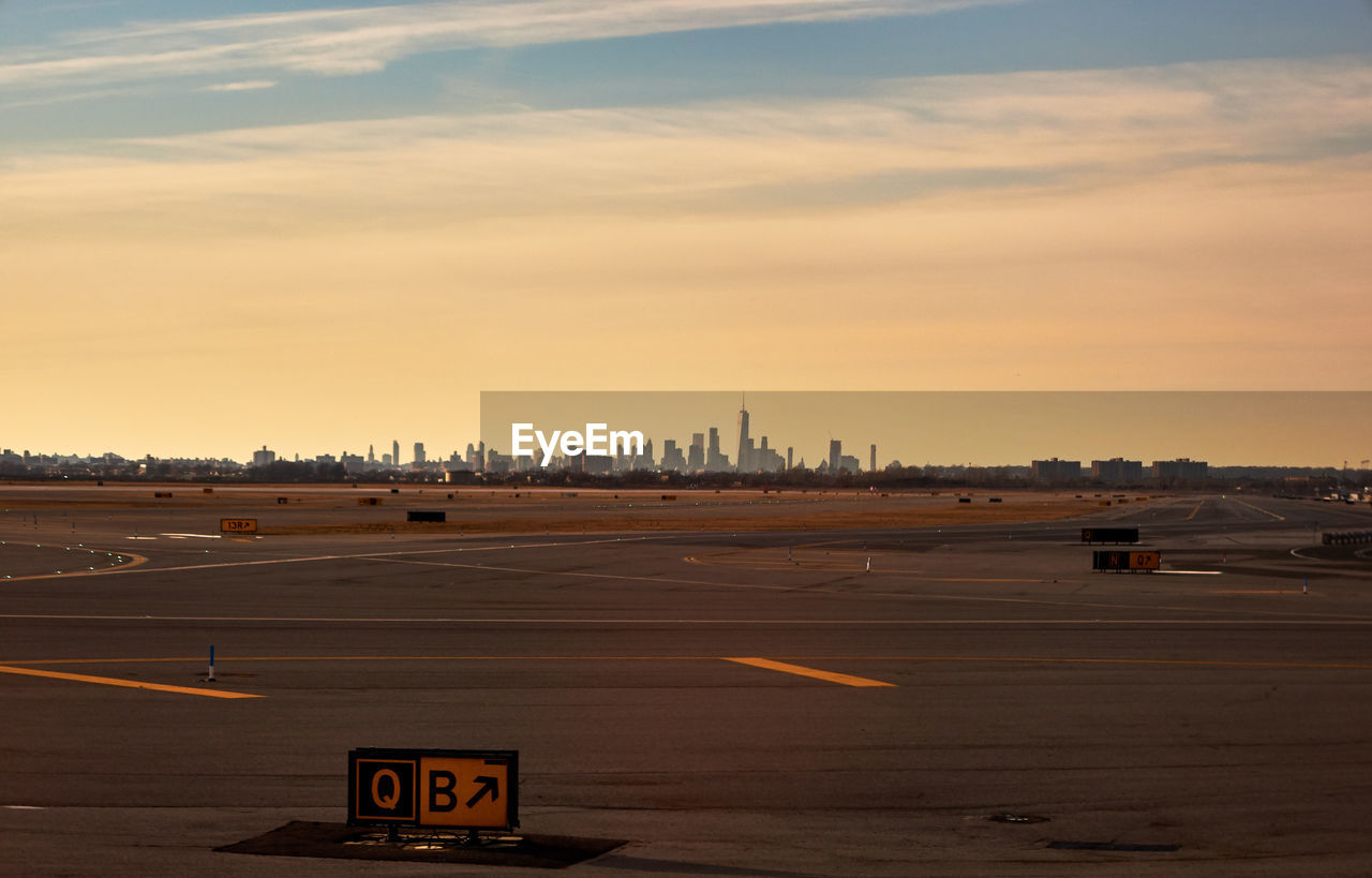 Empty runway in city against sky during sunset