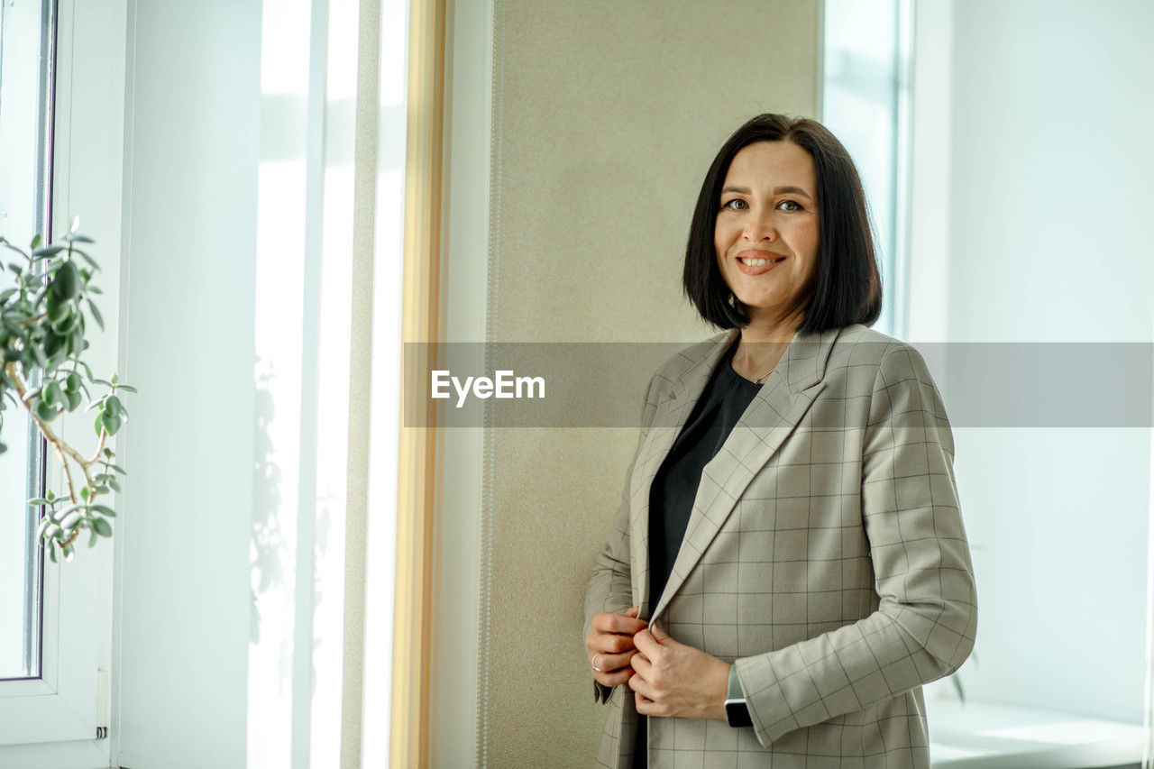 Smiling business. smiling businesswoman. entrepreneur stands in jacket in office lobby by the window