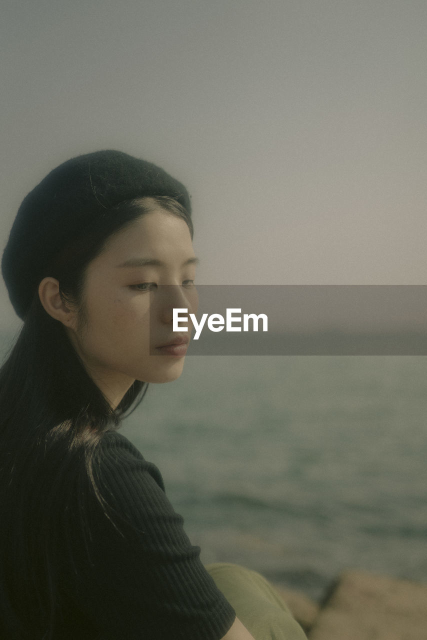 PORTRAIT OF BEAUTIFUL YOUNG WOMAN LOOKING AWAY AGAINST SEA