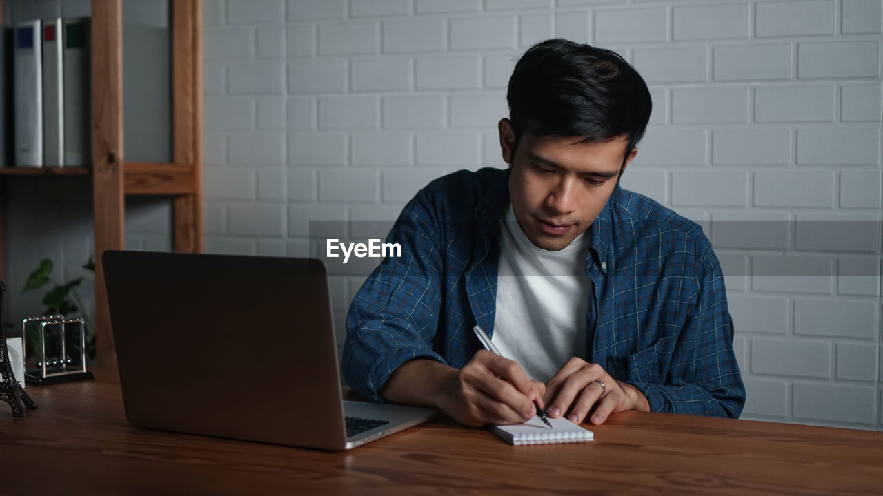 YOUNG MAN USING MOBILE PHONE AT TABLE