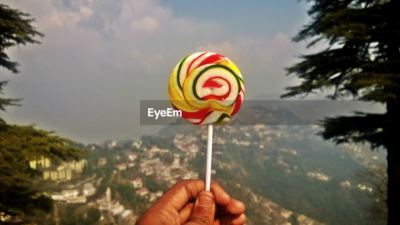 Cropped hand holding lollipop against mountain
