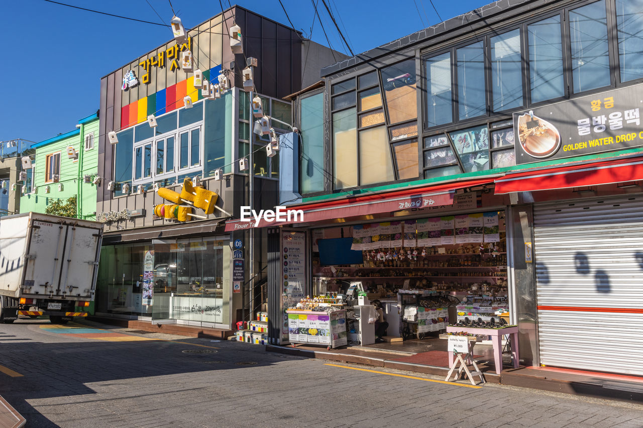 architecture, building exterior, city, built structure, urban area, street, downtown, road, town, neighbourhood, transportation, store, travel destinations, day, business, sign, text, building, nature, no people, transport, sky, outdoors, city street, communication, facade, mode of transportation, travel, city life, commercial sign, cafe, restaurant, clear sky, footpath