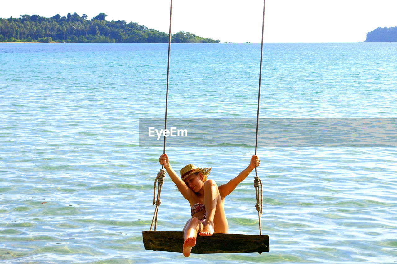 Woman swinging over sea against clear sky