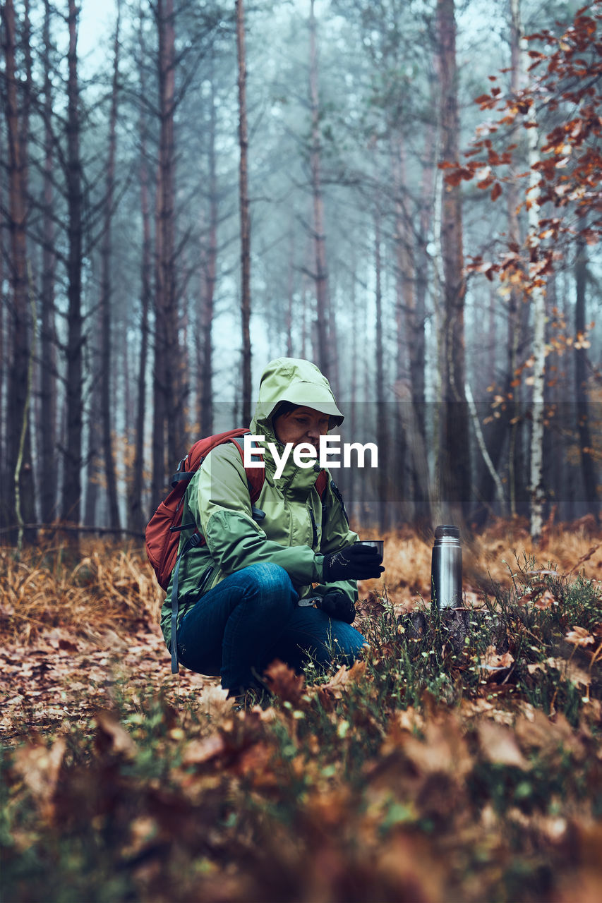 Woman with backpack having break during autumn trip drinking a hot drink from thermos flask