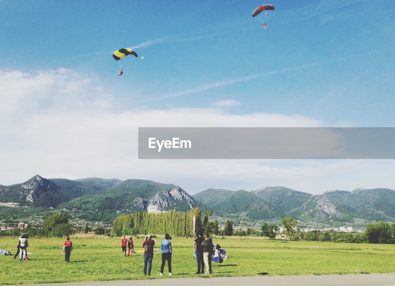 Paragliders flying over people standing on grass field