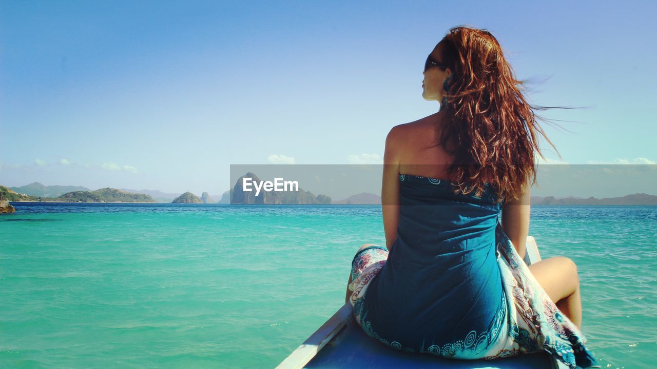 Rare view of young woman sitting on wooden structure on sea against sky