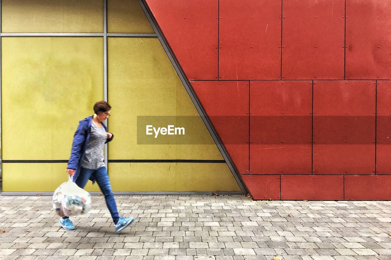 Side view of woman with polyethene bag walking on footpath