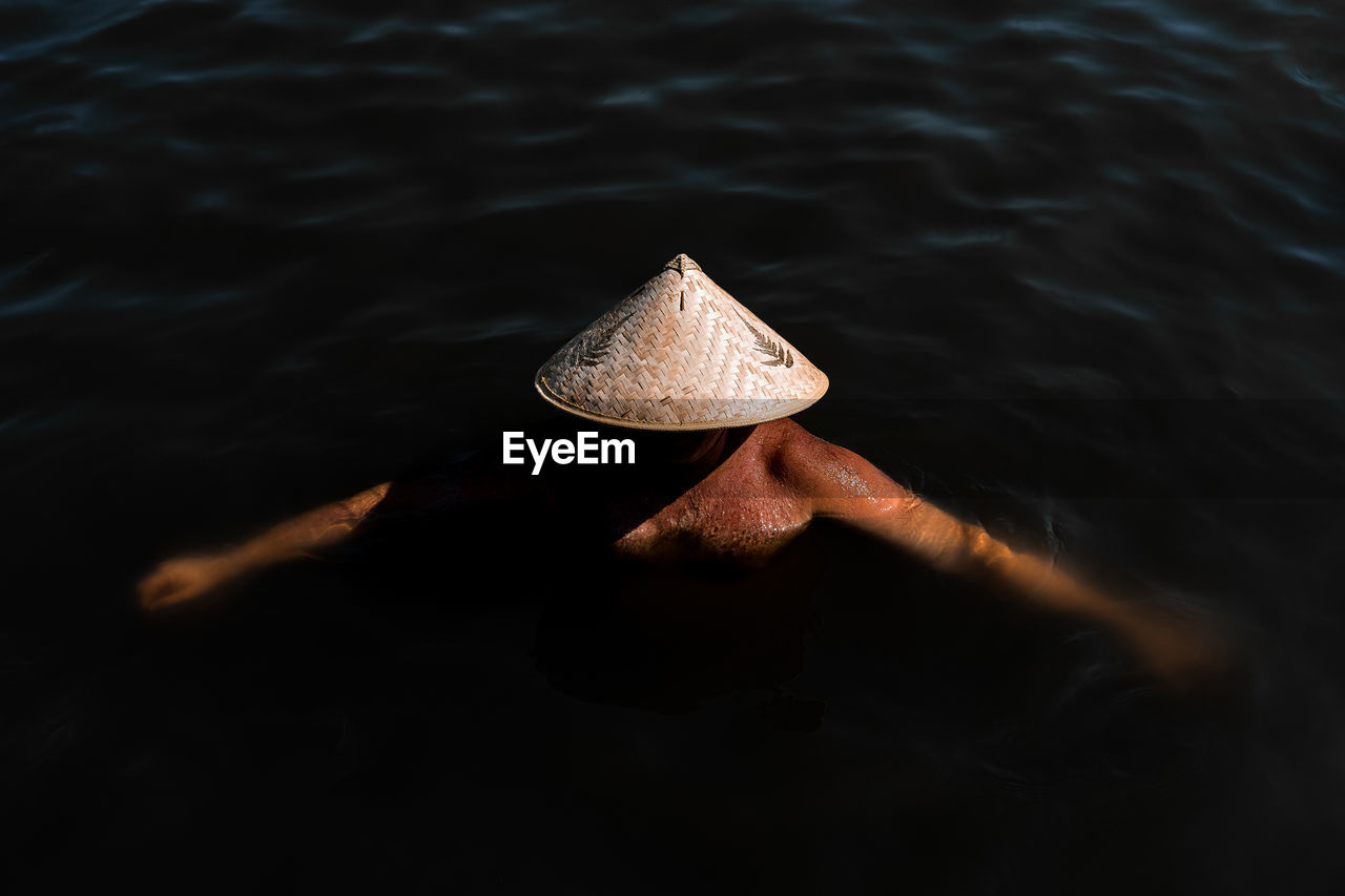 High angle view of man wearing asian style conical hat while swimming in sea