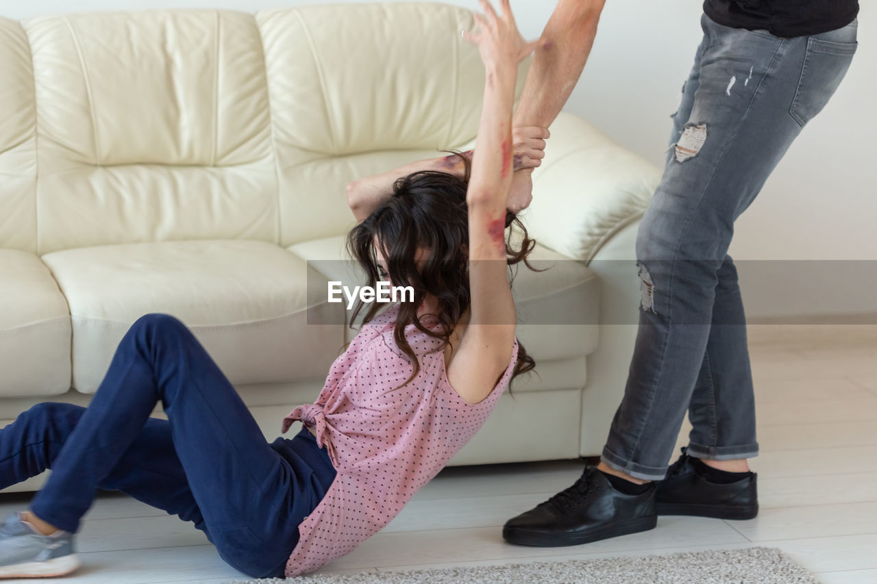 Low section of friends sitting on sofa at home