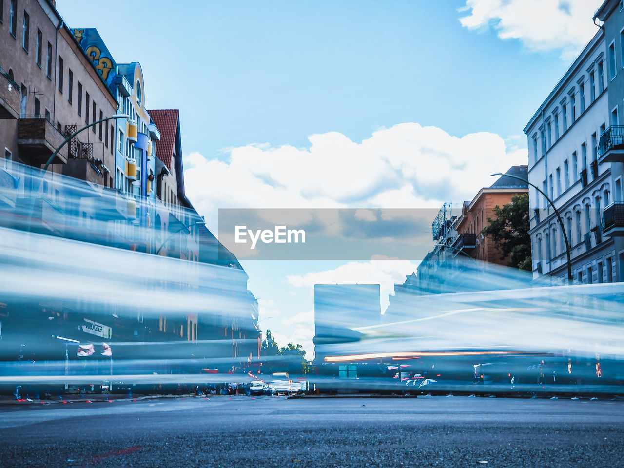 LIGHT TRAILS ON ROAD BY BUILDINGS AGAINST SKY