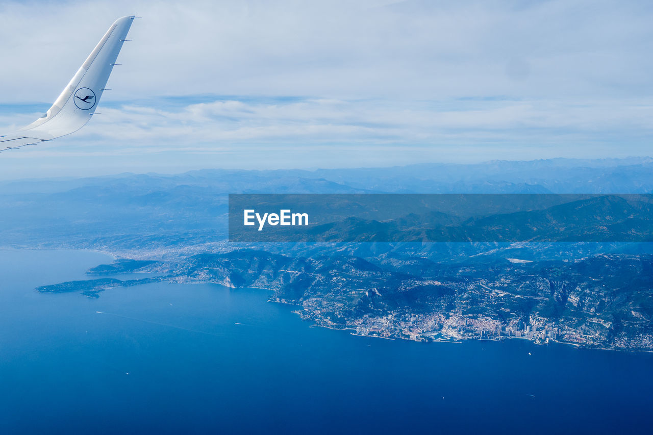 airplane, aerial view, air vehicle, water, transportation, sky, environment, cloud, travel, nature, flying, mode of transportation, scenics - nature, aircraft wing, beauty in nature, sea, landscape, horizon, no people, blue, aerial photography, mountain, travel destinations, outdoors, day, mountain range, vehicle, tranquility, tranquil scene, land, journey, reflection, mid-air