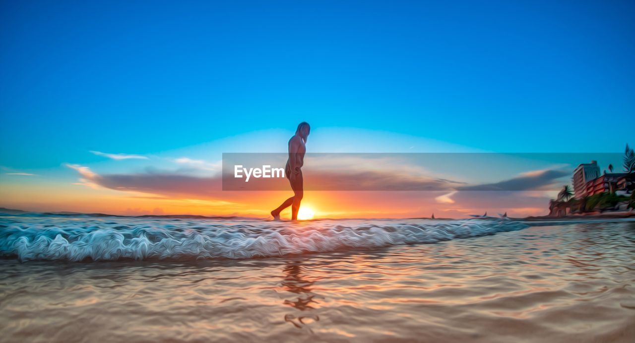 WOMAN STANDING AT SEA SHORE AGAINST BLUE SKY