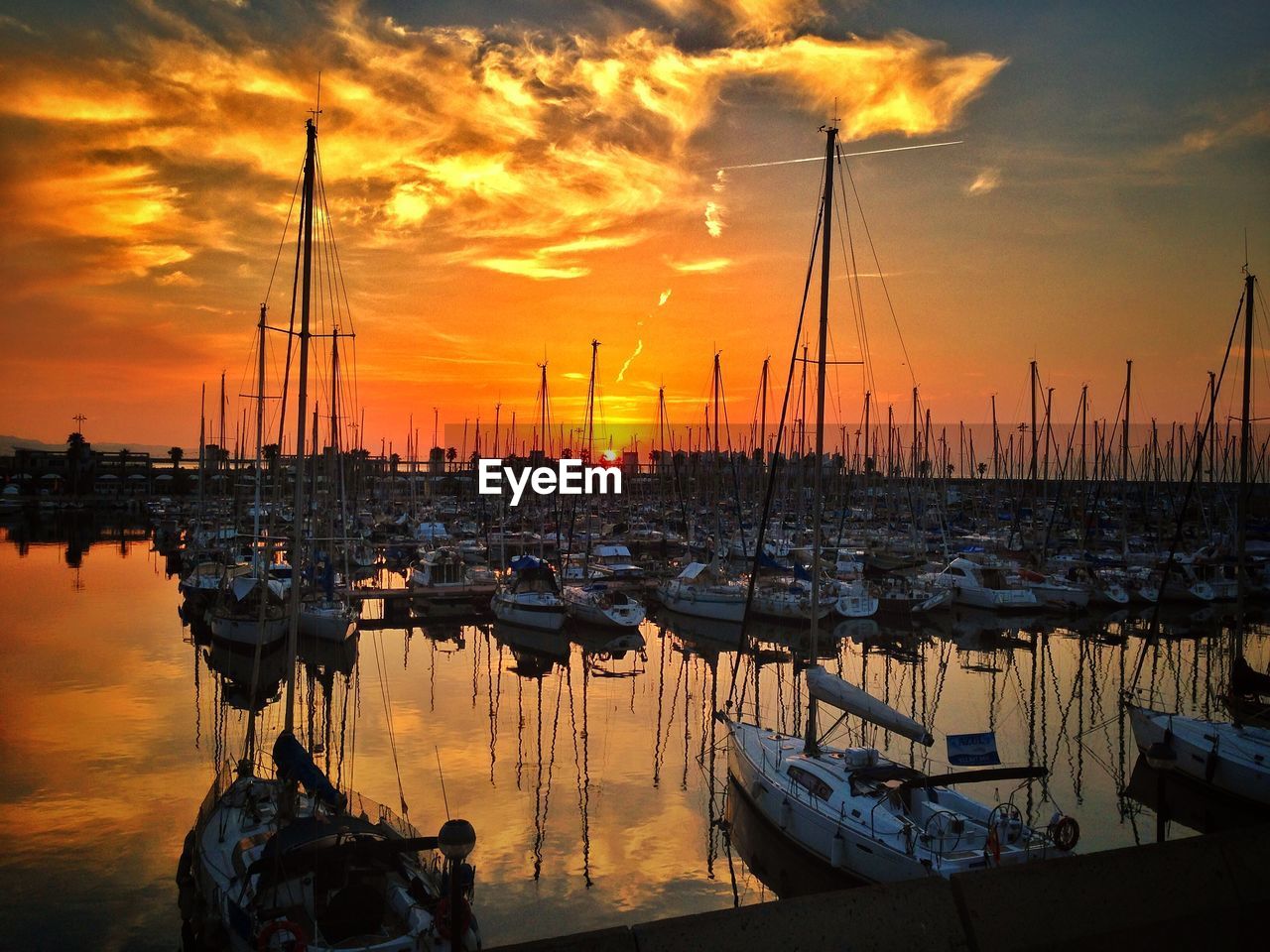 Boats moored at harbor in sea against orange sunset sky