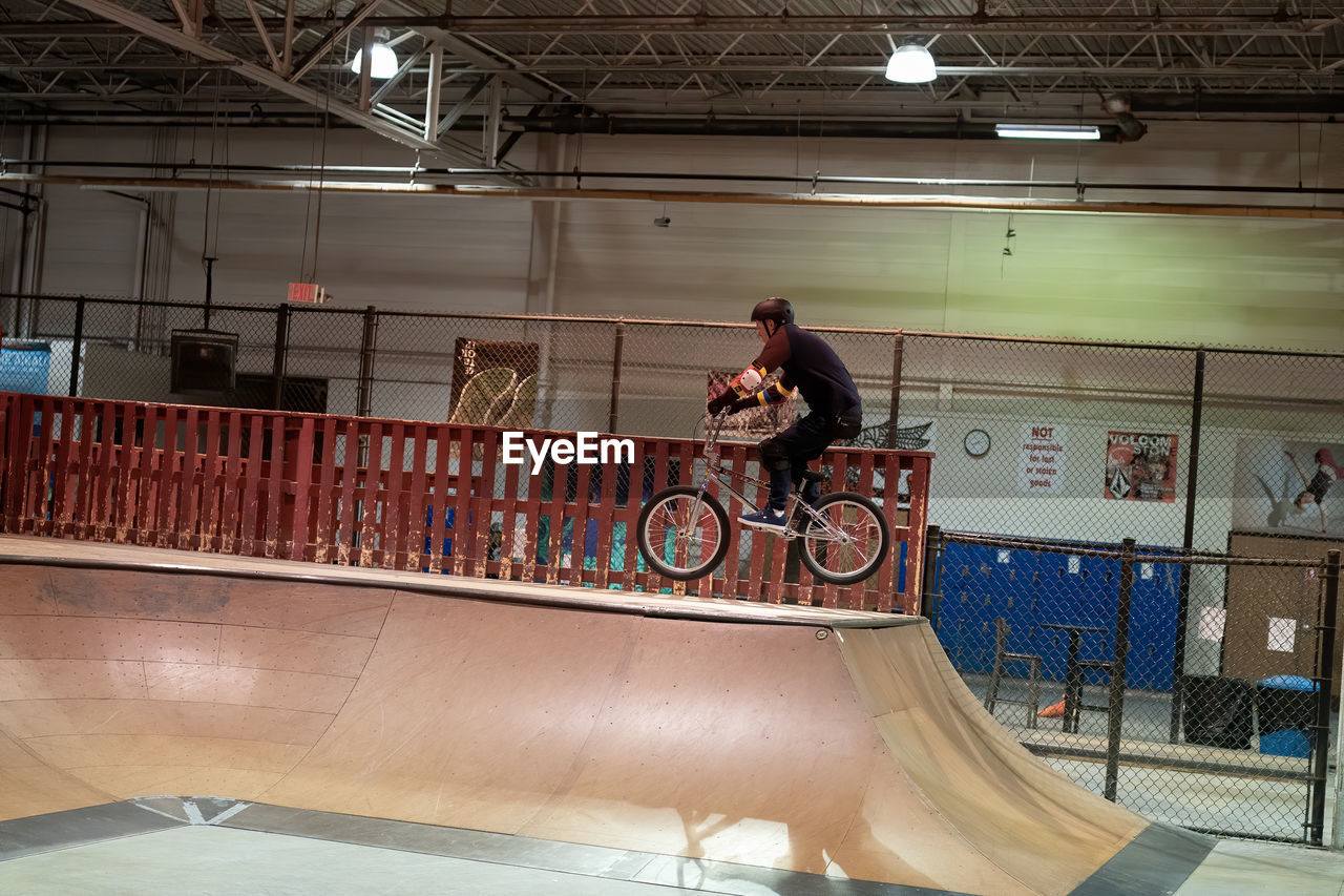 MAN RIDING BICYCLE ON RAILING AGAINST BRIDGE