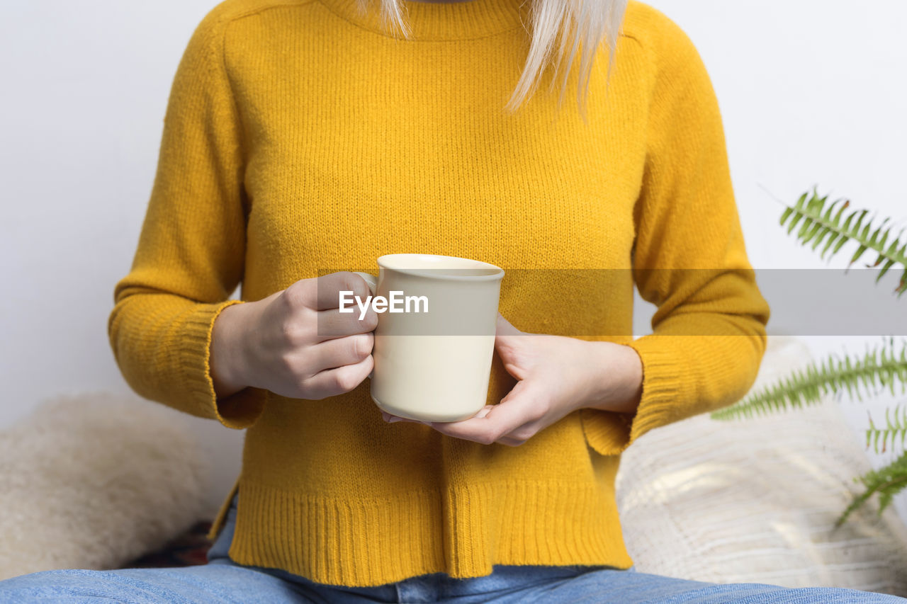 Midsection of woman holding coffee cup against wall