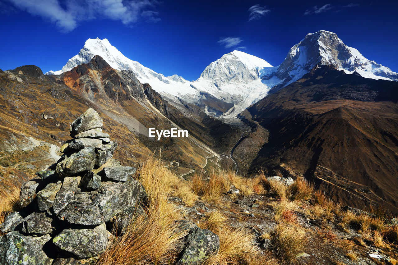 Heap of stone by dry grass with mountains in background against sky