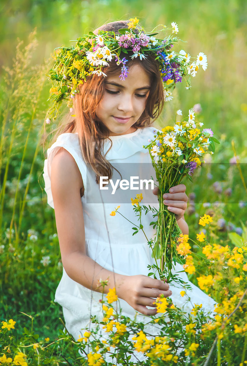 Girl wearing floral crown holding flowers in meadow