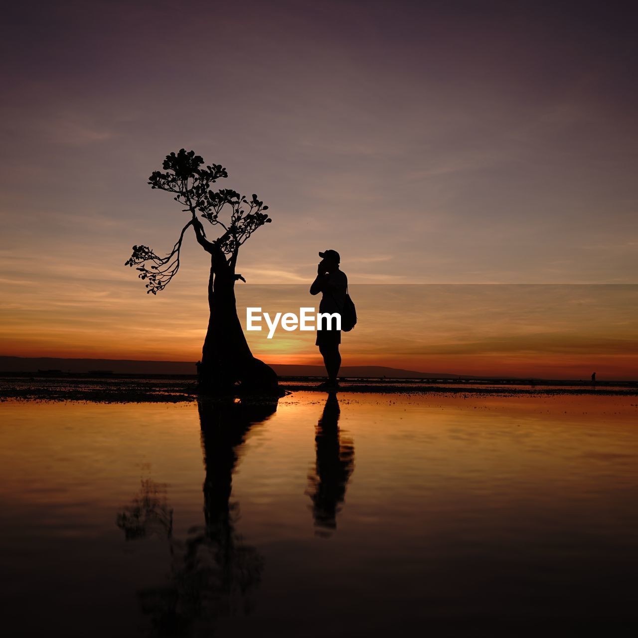 Silhouette man standing on shore against sky during sunset