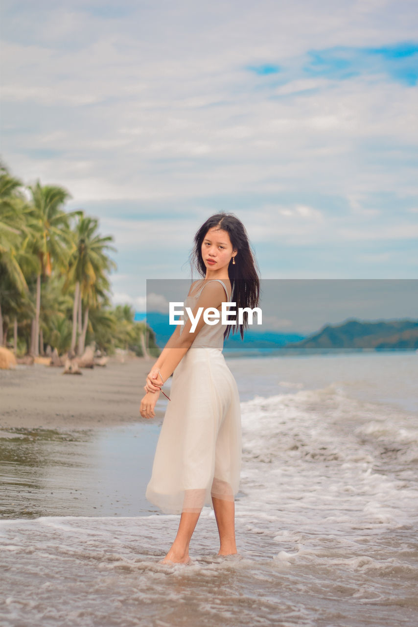 Portrait of woman standing on beach against sky.