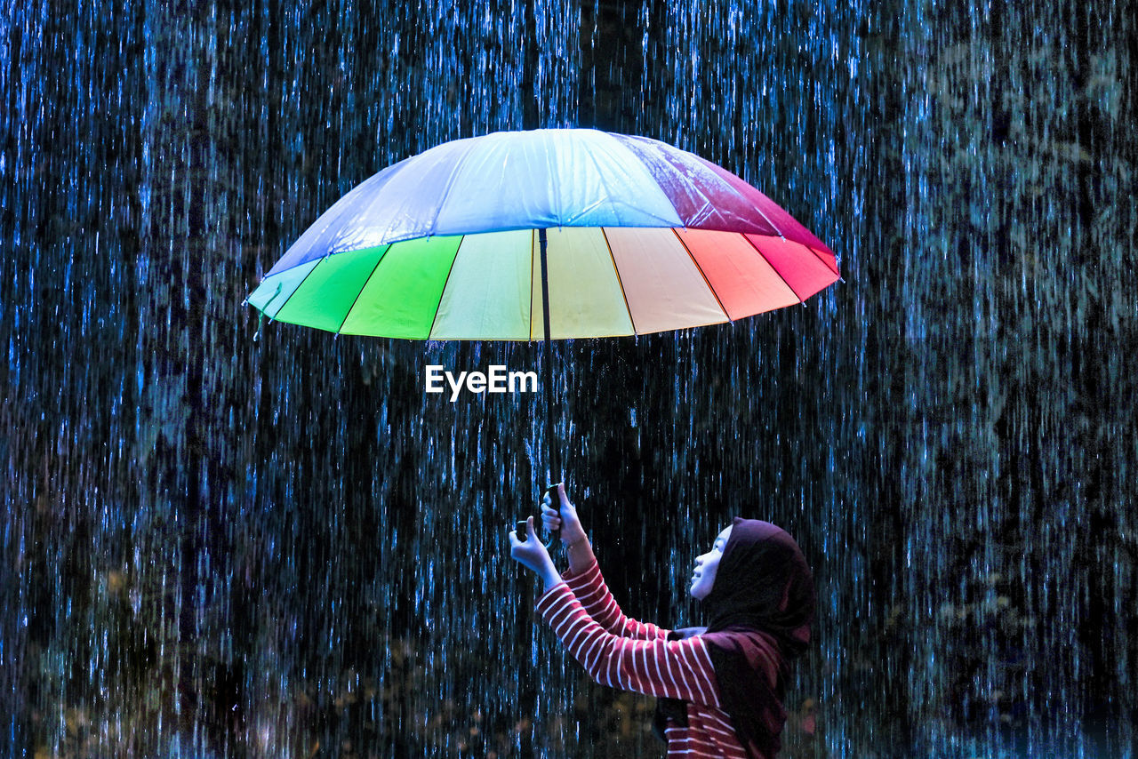 Teenage girl holding multi colored umbrella against rain