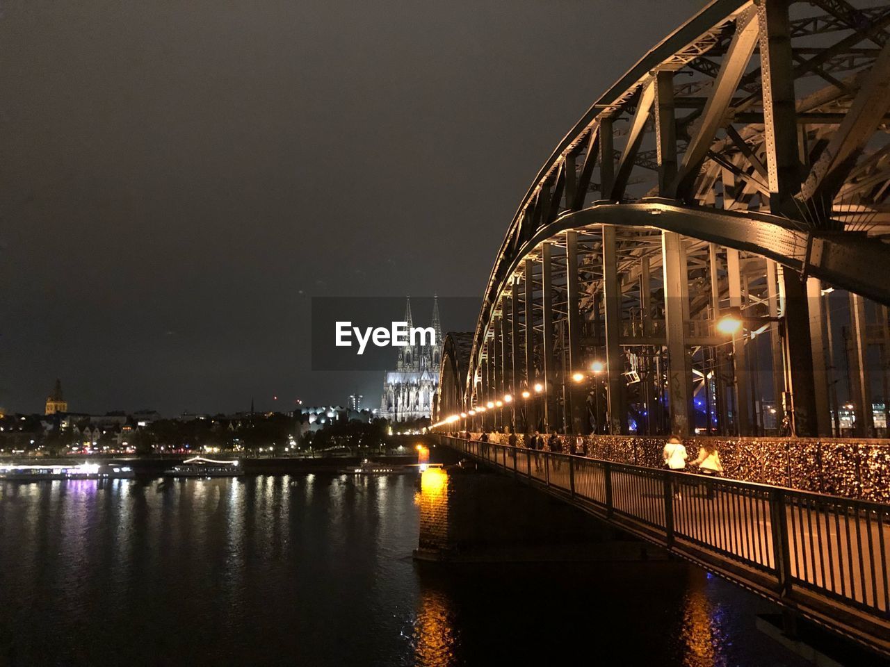 Illuminated bridge over river by buildings against sky at night