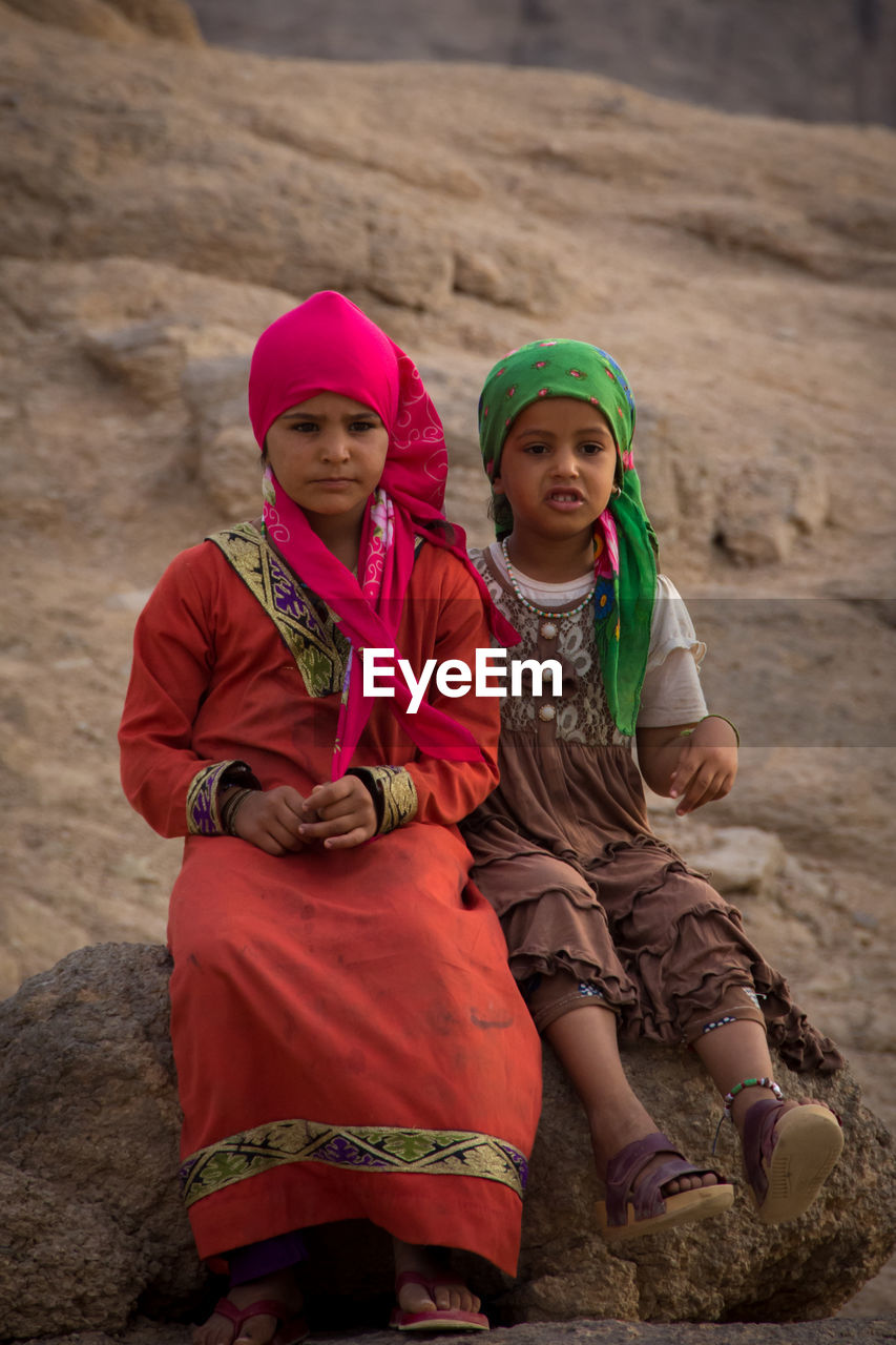 Thoughtful sisters wearing headscarves while sitting on rock