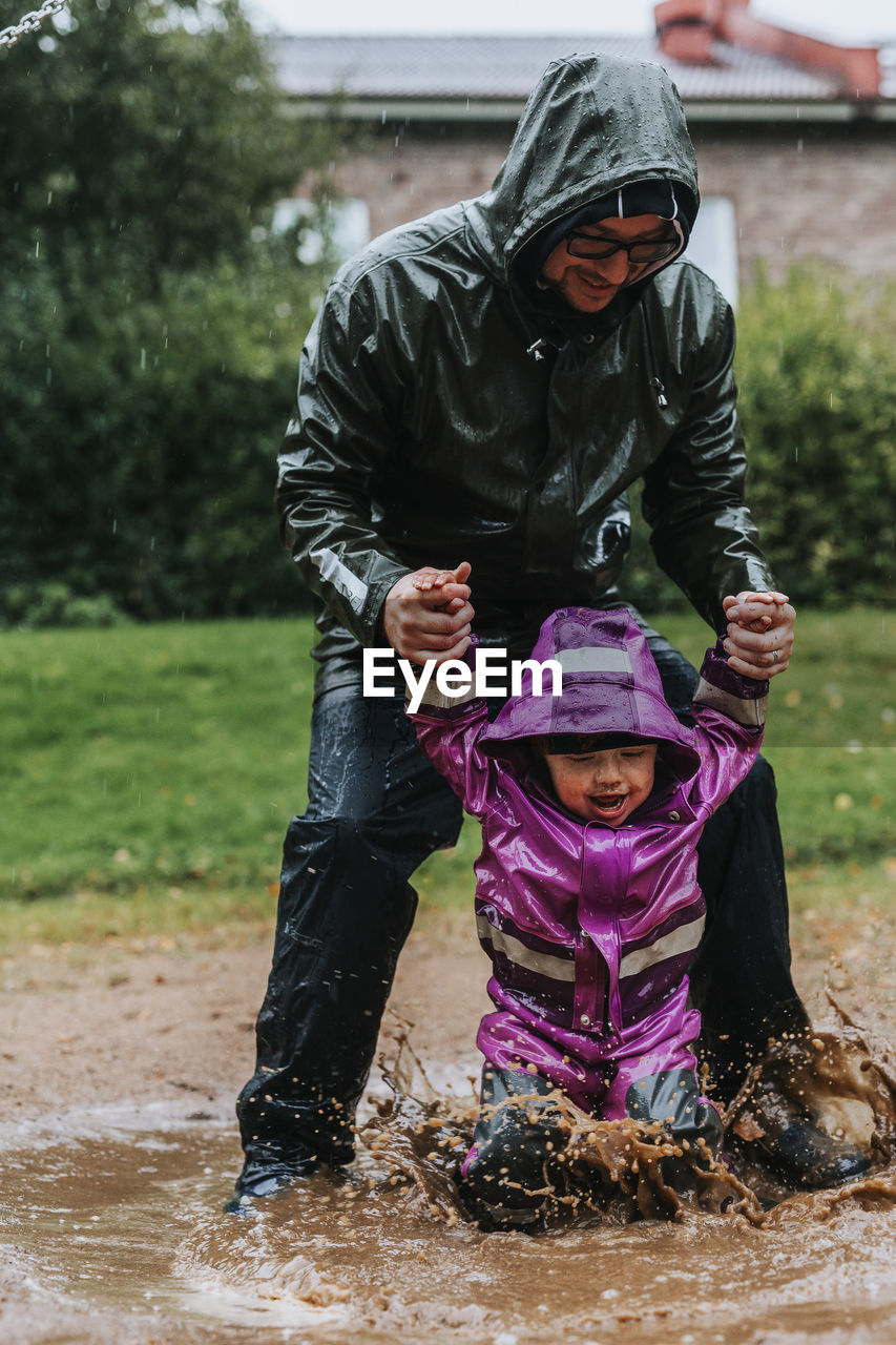 Father playing with toddler girl in puddle